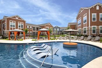An outdoor pool with chairs and umbrellas in front of an apartment building